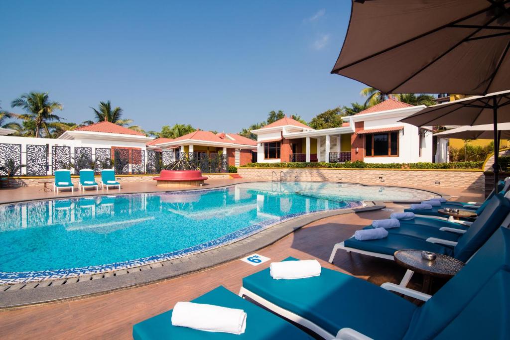 a swimming pool with blue lounge chairs and an umbrella at The Grand Leoney Resort in Vagator