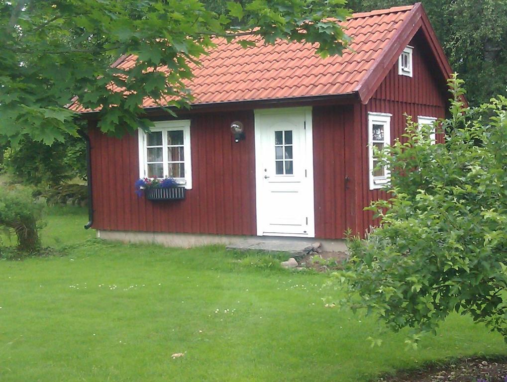 einen roten Schuppen mit einer weißen Tür und einem Fenster in der Unterkunft Stensholms Trädgård in Nässjö