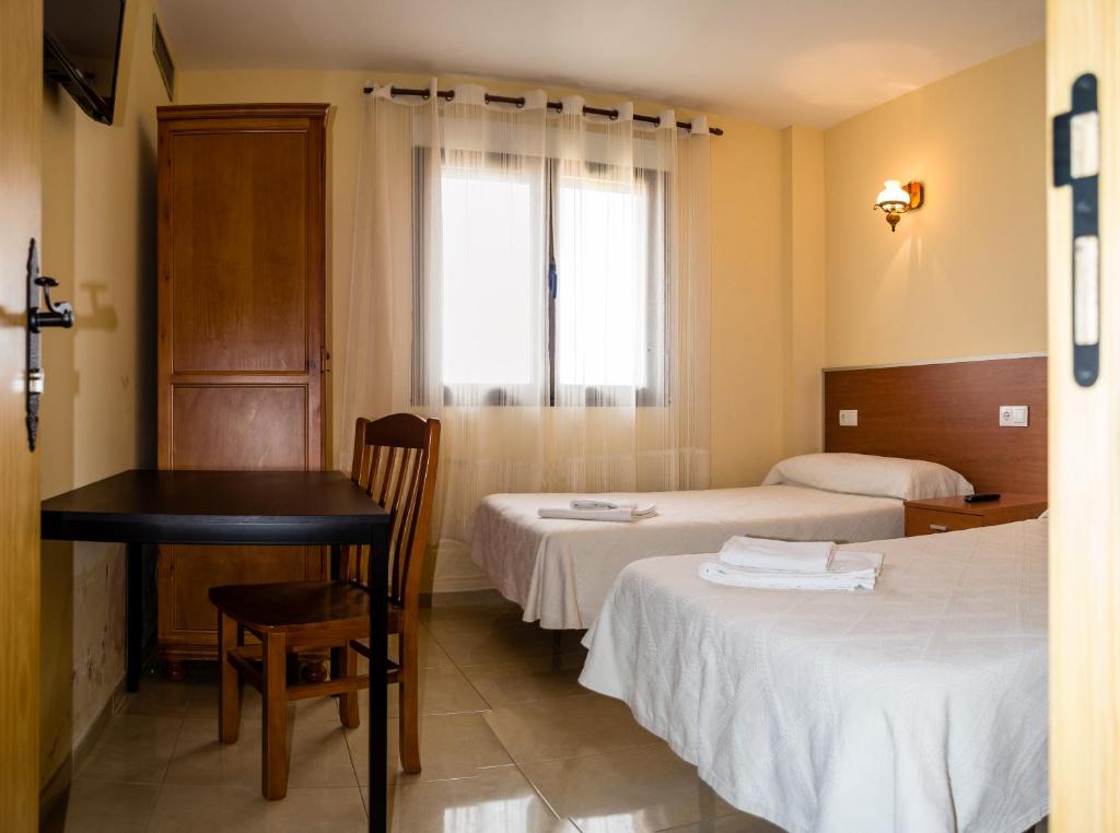 a room with two beds and a table and a window at El Roble Hotel Restaurante in Tábara