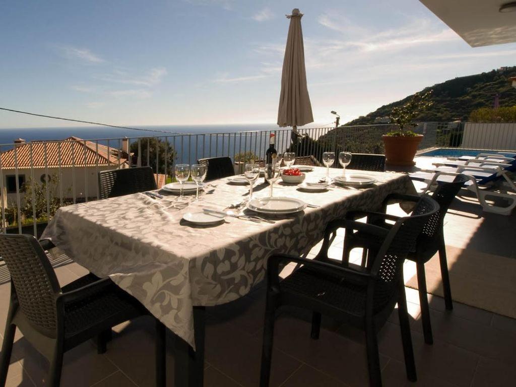 einen Tisch mit Weingläsern und Stühlen auf einer Terrasse in der Unterkunft Blue Villa in Arco da Calheta