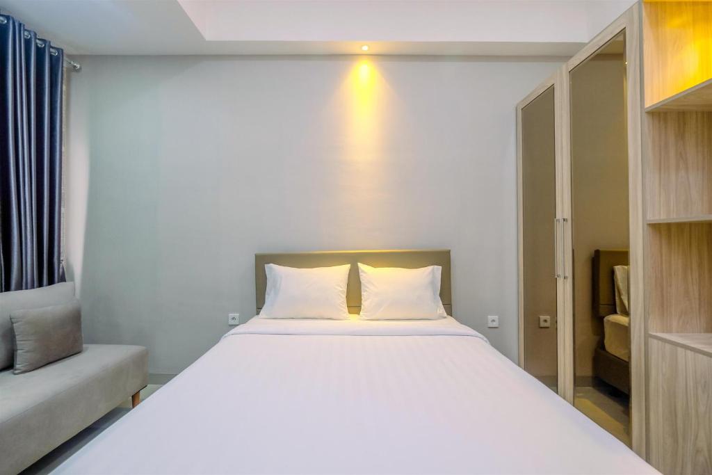 a bedroom with a large white bed and a couch at Homey and Warm Studio Apartment Oasis Cikarang By Travelio in Cikarang
