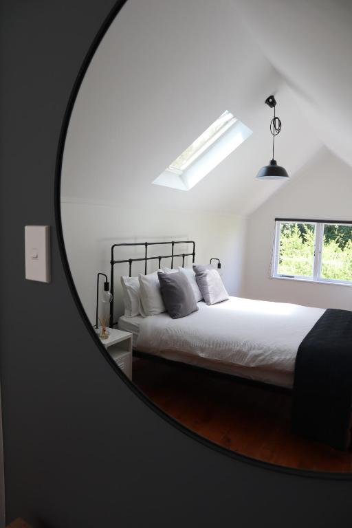 a mirror in a bedroom with a bed and a window at T H E B A R N Boutique Accomodation in Tauranga