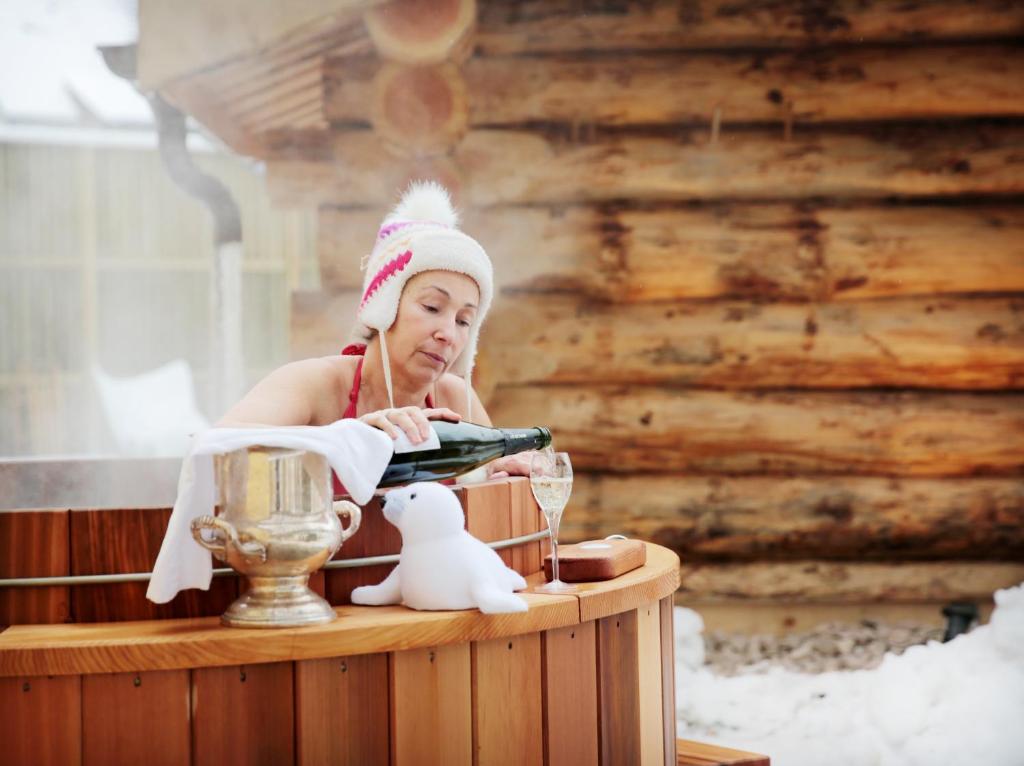 une femme assise dans une baignoire avec une bouteille de vin dans l'établissement Logis Hôtel Restaurant De La Poste et SPA de Montagne, à Le Bonhomme