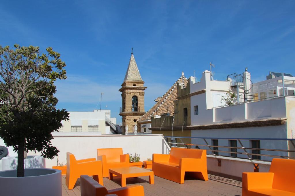 un balcón con sillas naranjas y una torre del reloj en Apartamentos Maier, en Cádiz