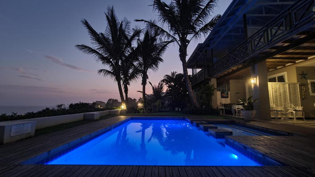 a swimming pool in front of a house with palm trees at Shaka's Seat Guesthouse - Check Out Our May Special! in Ballito