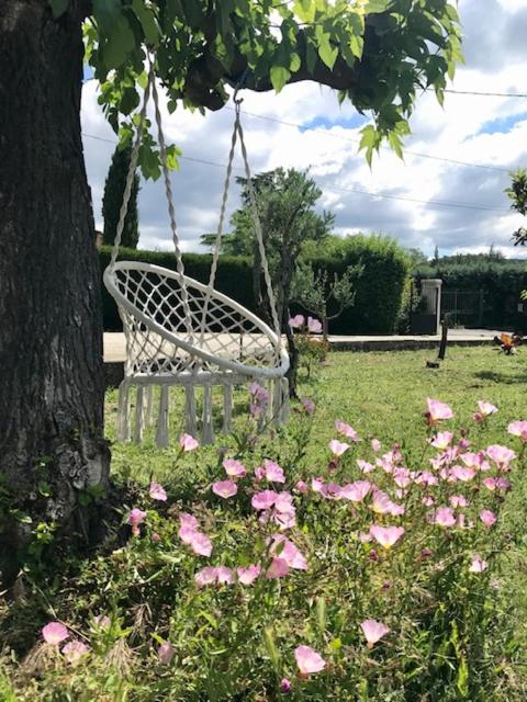 une balançoire suspendue à un arbre dans une cour ornée de fleurs roses dans l'établissement Occitemps, à Saint Julien Les Rosiers
