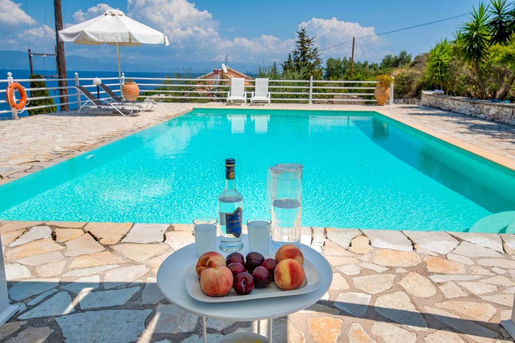 a plate of fruit and a bottle of wine next to a swimming pool at The Kantada Villas Petros, Eleni, Stelios & Dioni in Gaios