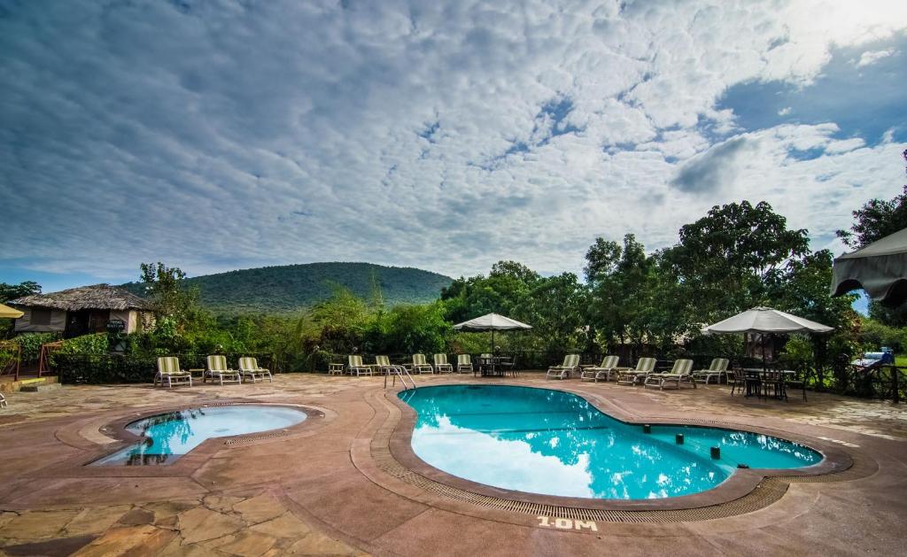 a swimming pool with chairs and tables and a mountain at Sentrim Mara Lodge in Ololaimutiek