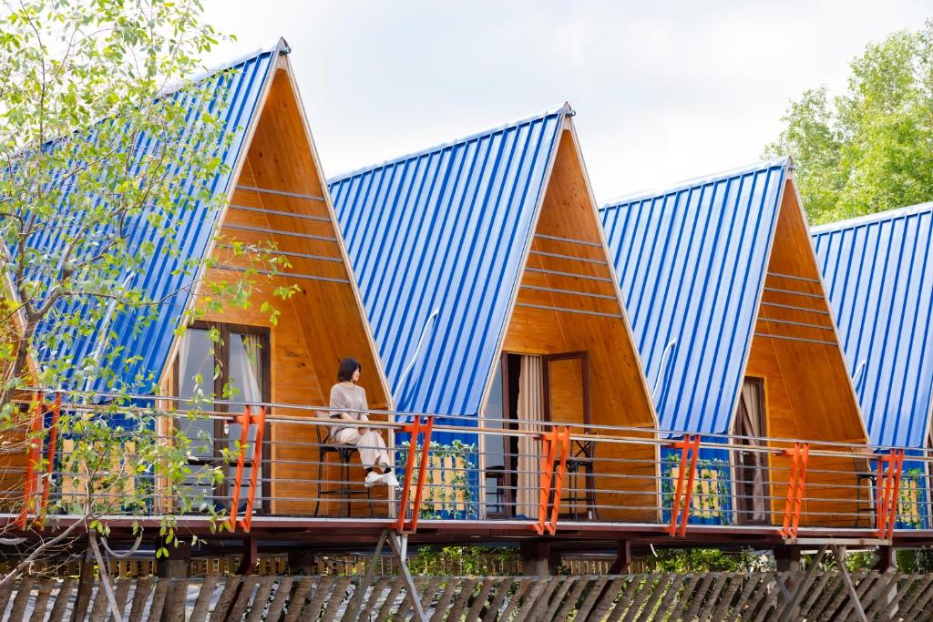 a house with a blue roof and a person sitting on a fence at S'Bungalow Bến Tre in Ben Tre