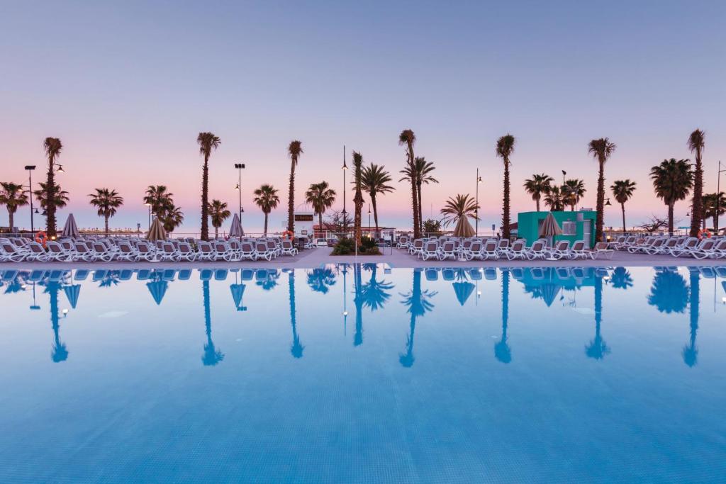 a swimming pool with chairs and palm trees at Hotel Riu Costa del Sol - All Inclusive in Torremolinos