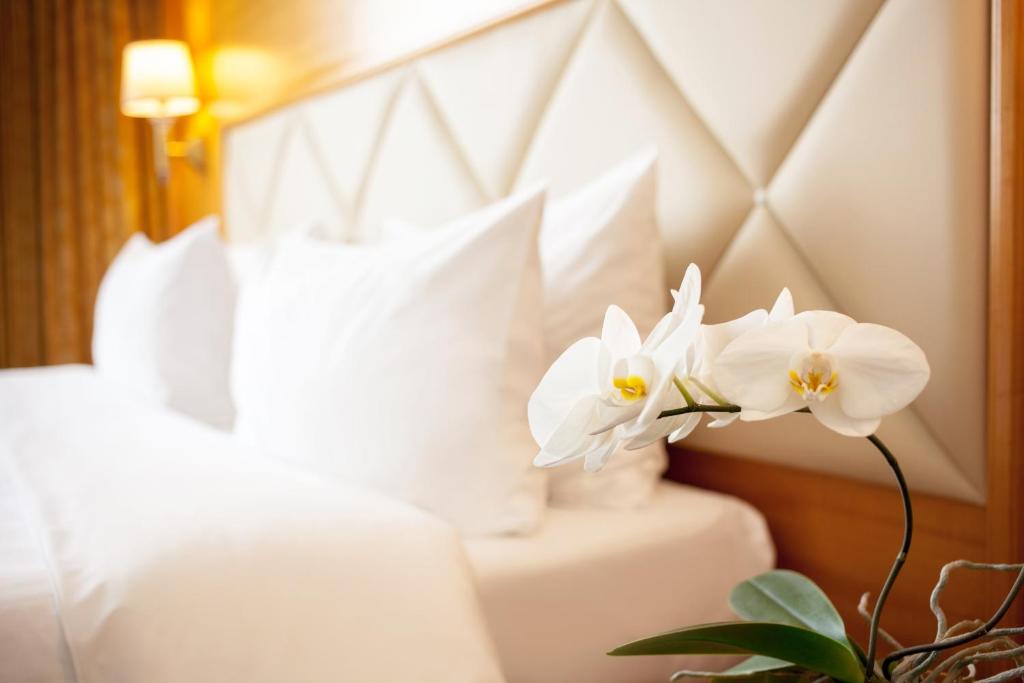 two white flowers in a vase on a bed at Milan Hotel Moscow in Moscow