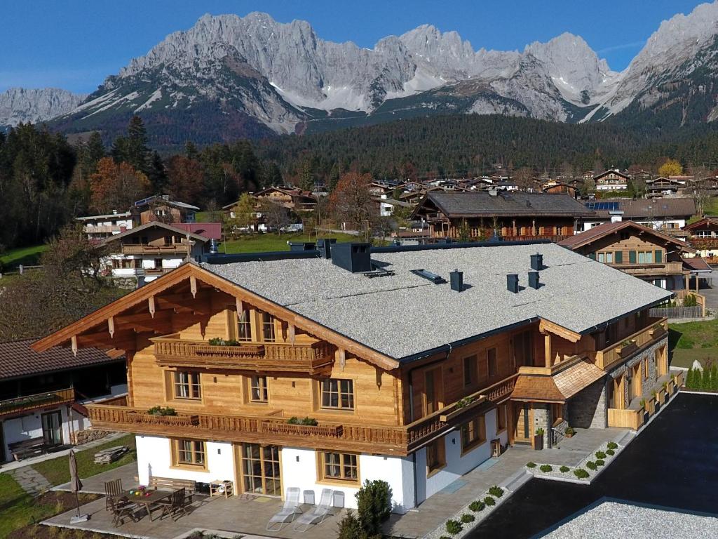 une grande maison en bois avec des montagnes en arrière-plan dans l'établissement Bichlhof Going, à Going am Wilden Kaiser