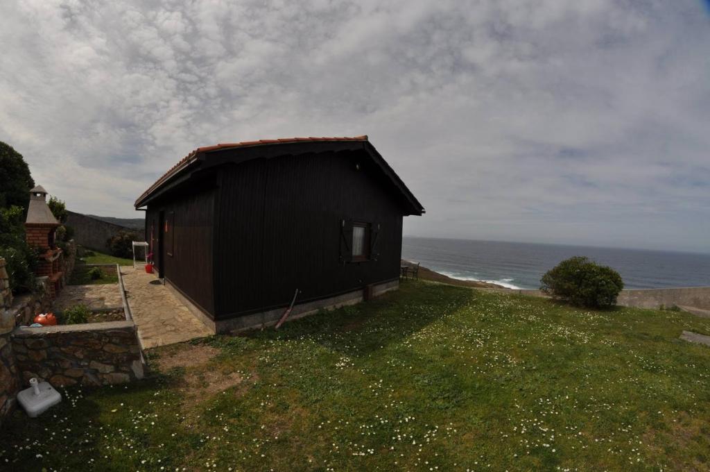 ein kleines schwarzes Gebäude auf der Seite des Ozeans in der Unterkunft Bungalow 1 - Playa Arnela in Carballo