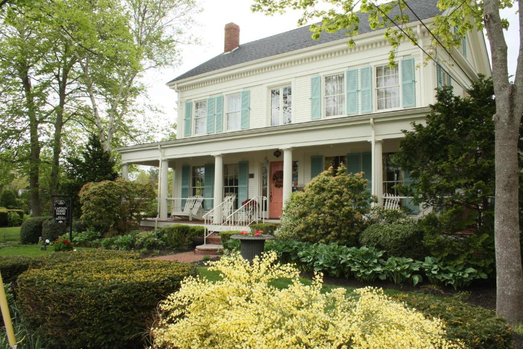 a white house with blue windows and bushes at Captain Farris House in South Yarmouth