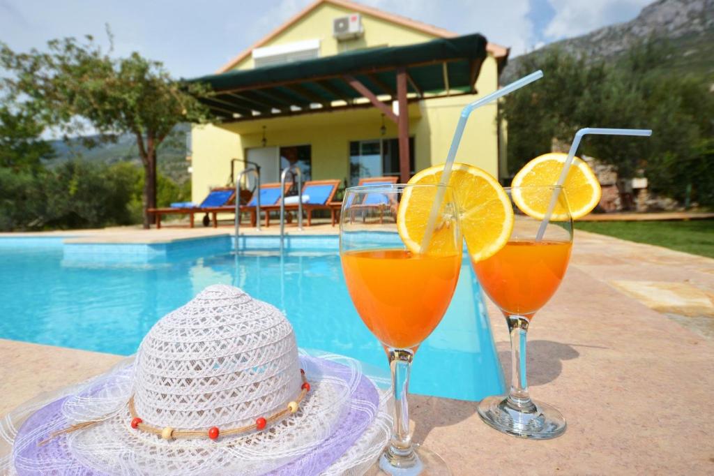 due bicchieri di succo d'arancia e un cappello accanto alla piscina di Holiday Home Nevenka a Kaštela (Castelli)