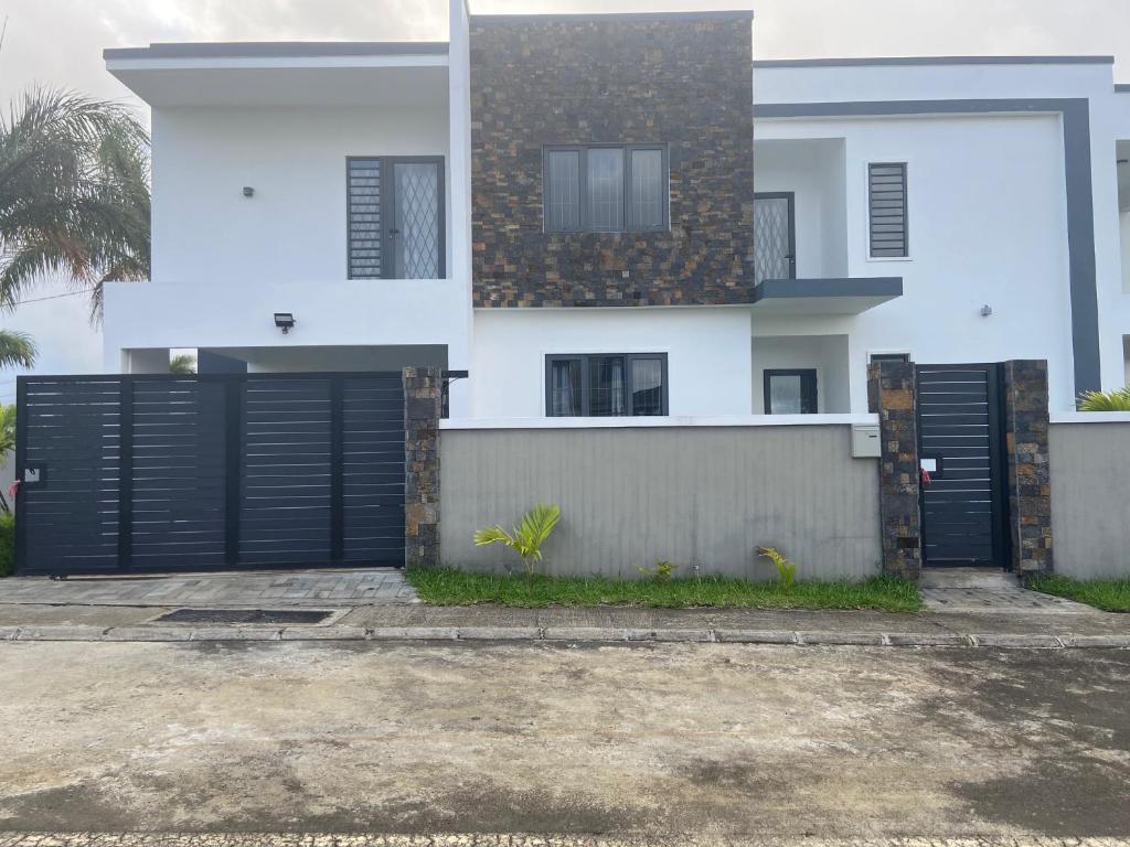 uma casa branca com portas de garagem pretas em frente em Kooshal Seetul House Villa - Room em Centre de Flacq