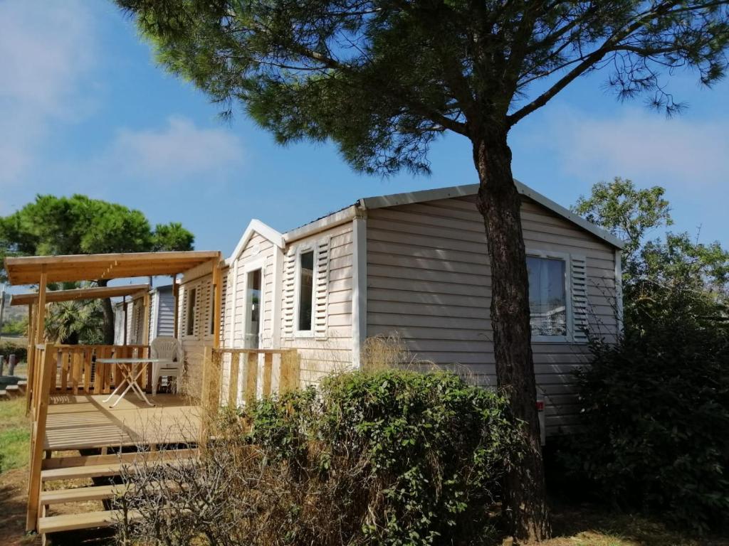 una casa pequeña con terraza y árbol en Mobil Home climatisé Camping Novella, en Port-la-Nouvelle