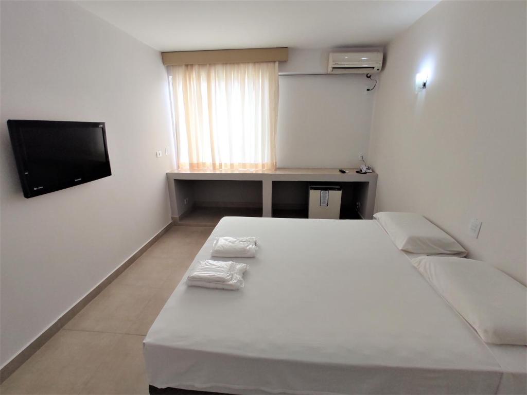 um quarto branco com uma cama e uma televisão em Manacá Hotel em Foz do Iguaçu