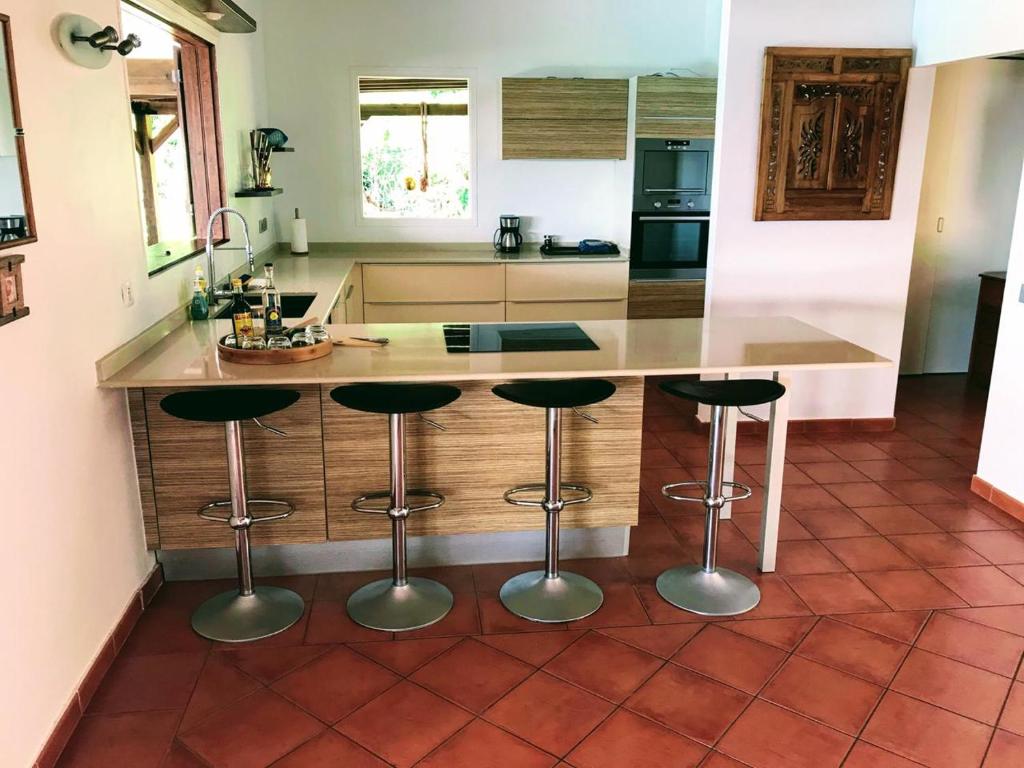 a kitchen with a counter with four bar stools at Villa Libellule in Grand-Bourg