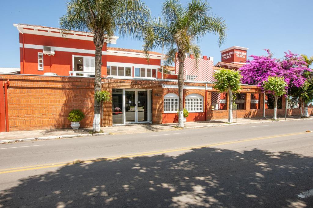 a red brick building on a street with palm trees at Hotel Pousada Casa Tasca in Bento Gonçalves