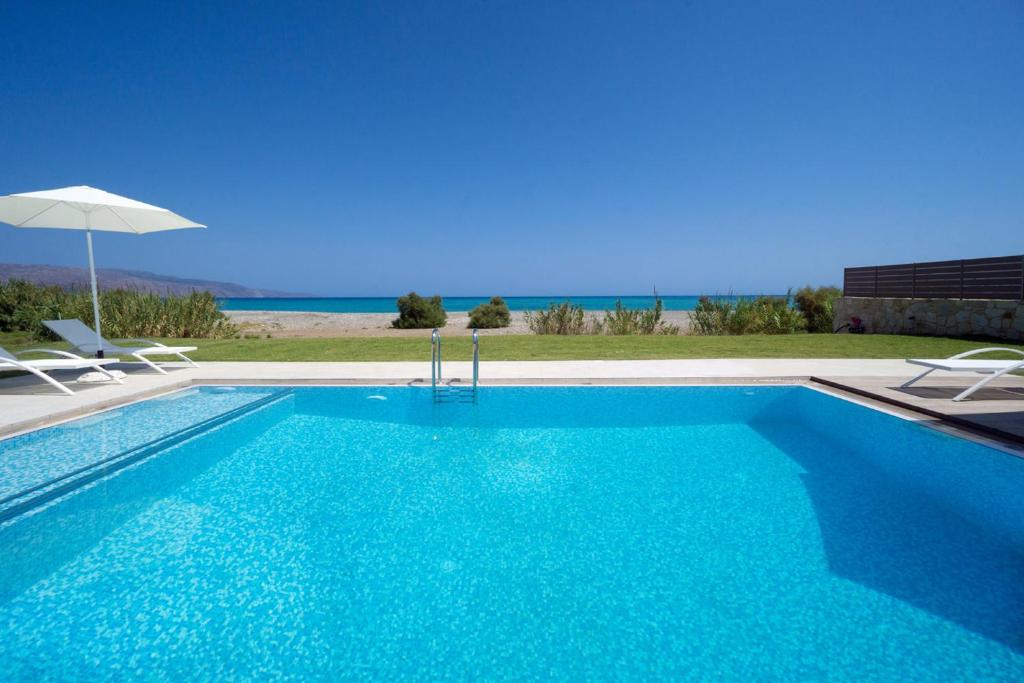 Una piscina con sillas y sombrilla y el océano. en Beach Villas, en La Canea