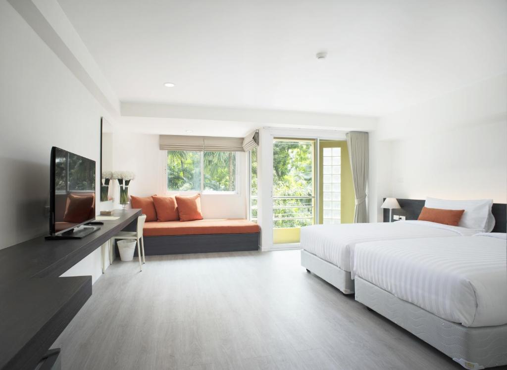 A bright bedroom with two beds, a sofa, television and a balcony door.