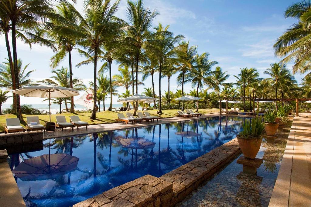 uma piscina com cadeiras e guarda-sóis e palmeiras em Txai Resort em Itacaré