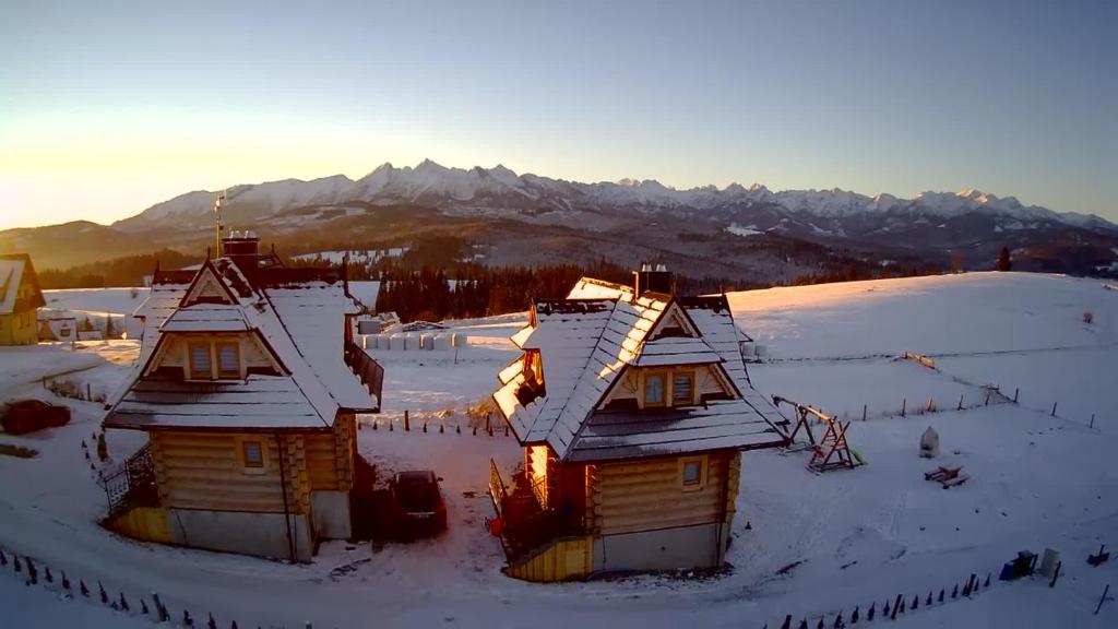 zwei schneebedeckte Häuser mit Bergen im Hintergrund in der Unterkunft Domki Pod Tatrami in Rzepiska