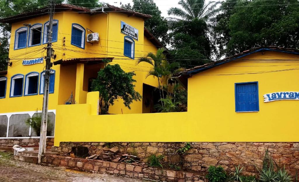 a yellow house with blue windows and a stone wall at Pousada Lavramor in Lençóis