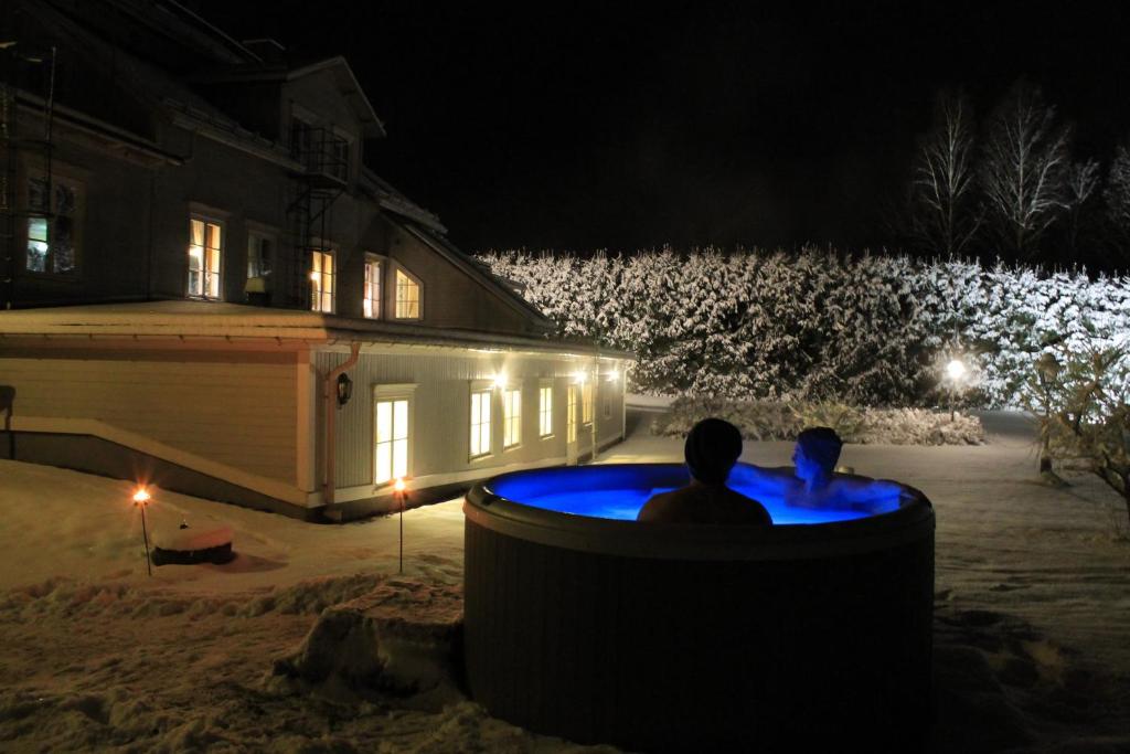 two people sitting in a hot tub in front of a house at night at Wanbo Herrgård in Nedre Vanbo