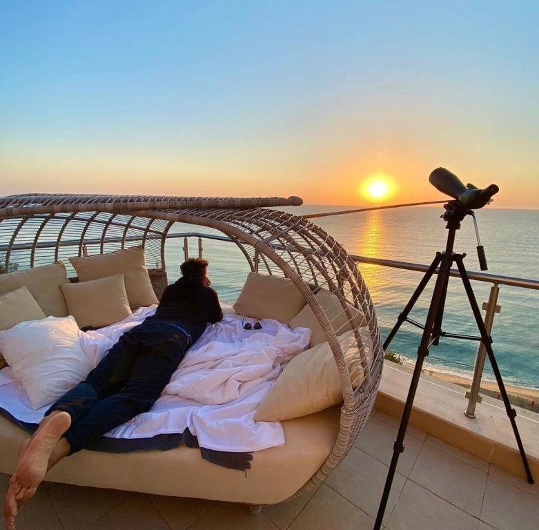 a man laying on a bed on a balcony with a camera at Бяла Виста Клиф - Byala Vista Cliff in Byala