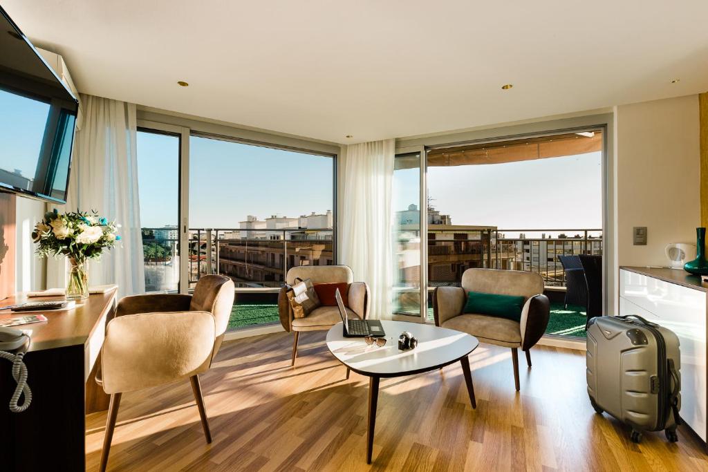 a living room with a table and chairs and windows at Hôtel Hélios in Juan-les-Pins