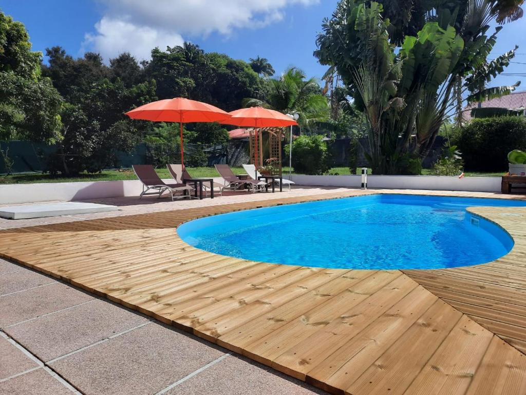 een zwembad met een houten terras en parasols bij Tropical Dream - Gîte Touristique - 4Adultes et 3Enfants in Baie-Mahault
