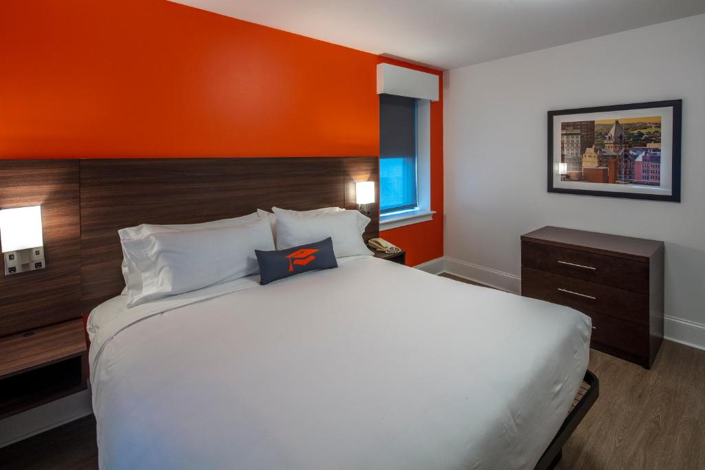 a bedroom with a large bed with an orange wall at Collegian Hotel & Suites, Trademark Collection by Wyndham in Syracuse
