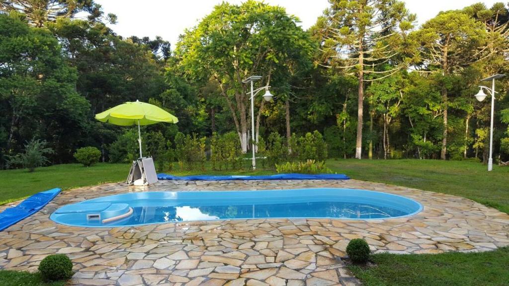 a swimming pool with an umbrella in a yard at Chacara maravilhosa pertinho de Curitiba in Curitiba