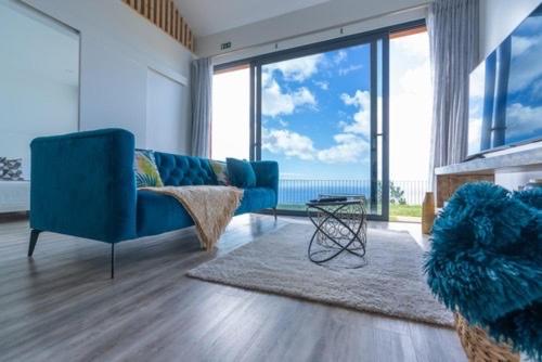 a living room with a blue couch and large windows at northsouthviescasinha in Calheta