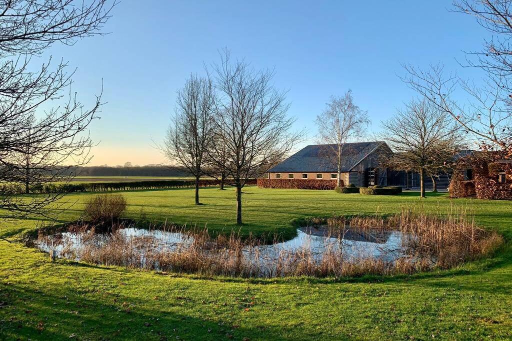 einen Teich inmitten eines Feldes mit einem Haus in der Unterkunft Karibu de Stallen (met Sauna en Stoom douche) in Daarle