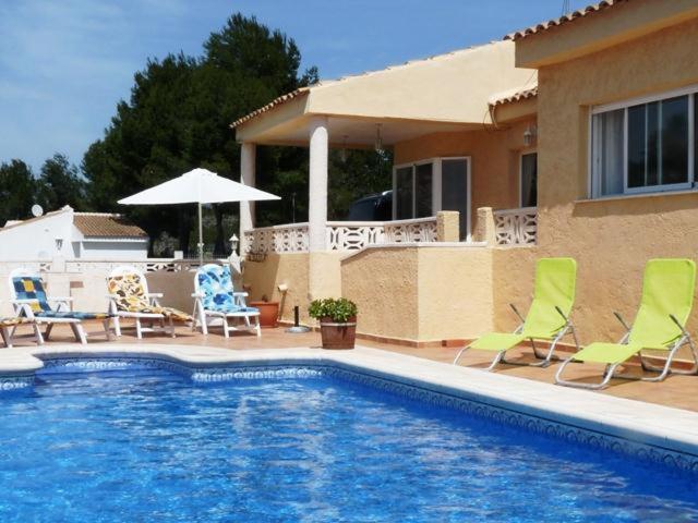 a swimming pool in front of a house with chairs and an umbrella at Sierra Verde Polop in Polop