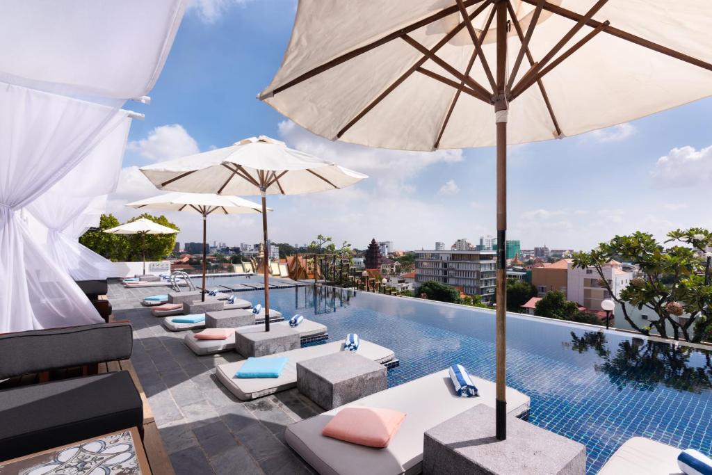 una piscina al aire libre con sombrillas, tumbonas y mesas en PATIO Hotel & Urban Resort, en Phnom Penh