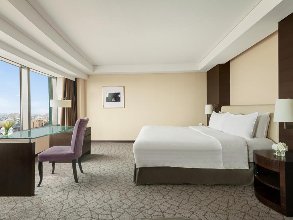a hotel room with a bed and a desk and a bed and a window at Shangri-La Far Eastern Tainan in Tainan
