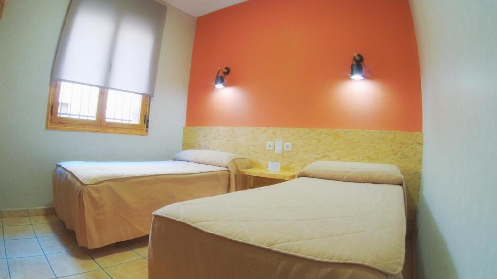 2 camas en una habitación con pared de color naranja en Hs San Francisco - CÉNTRICO, en Almagro
