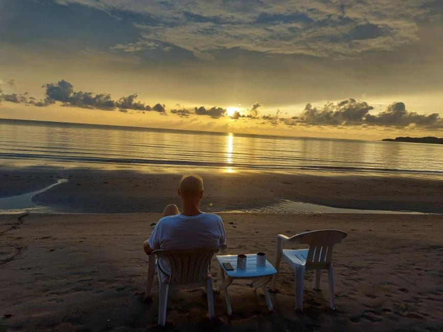 Ein Mann sitzt am Strand und sieht den Sonnenuntergang. in der Unterkunft Bella's Beach Resort Apartment 8 in Bauang