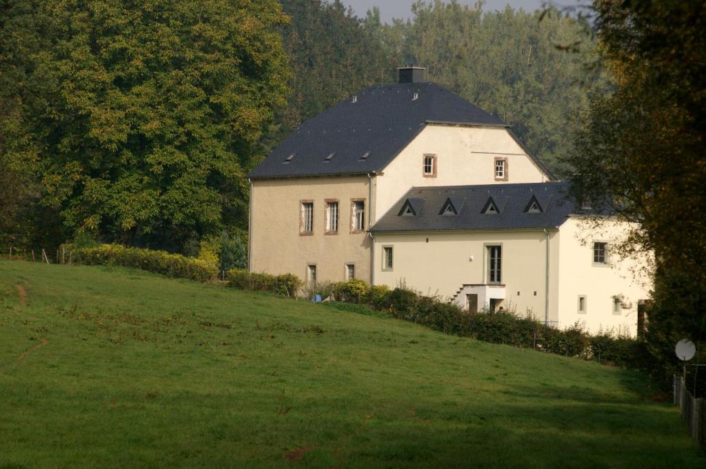 uma grande casa branca com um telhado preto num campo em Bleesmillen em Diekirch