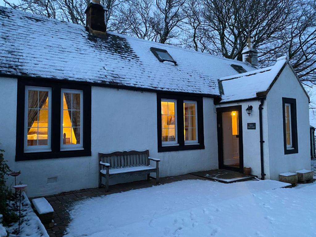 a white house with a bench in the snow at Shiel Cottage in Thornhill