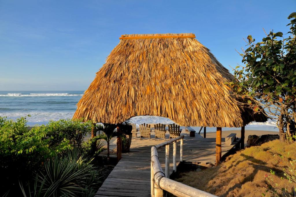 un camino de madera a una playa con una cabaña de paja en Hotel Posada Los Destiladeros en Pedasí Town