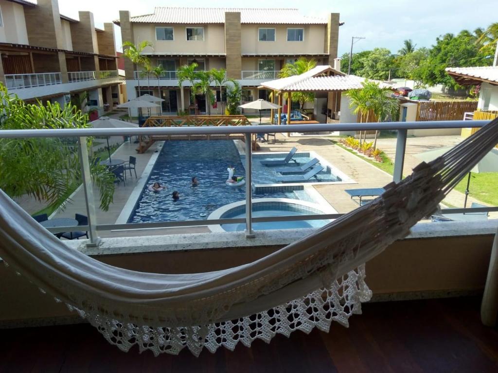 a hammock on the balcony of a resort with a pool at Village Praia do Surf, Itacimirim - Camaçari, BA in Itacimirim