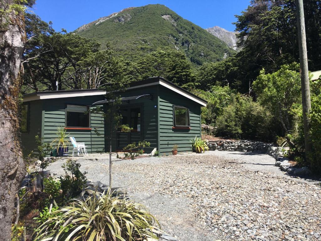 a green cabin with a mountain in the background at Petes Place in Arthur's Pass