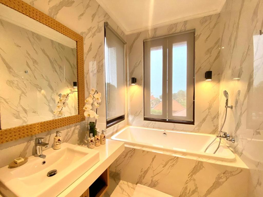 een badkamer met een bad, een wastafel en een spiegel bij Kayangan Boutique Hotel in Sanur