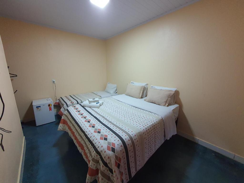 um pequeno quarto com uma cama com lençóis brancos e almofadas em Pousada Quatro Estações em Alto Paraíso de Goiás