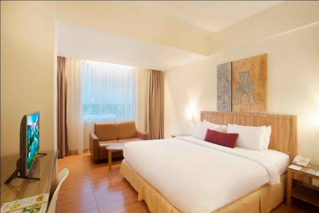 a hotel room with a large bed and a television at Grand Zuri Dumai in Dumai
